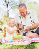 Grandfather and Granddaughter Coloring Easter Eggs on Blanket At