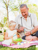 Grandfather and Granddaughter Coloring Easter Eggs on Blanket At