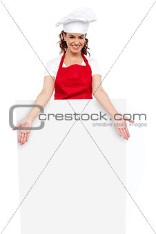 Female chef posing behind blank white billboard