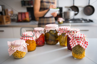 Closeup on jars of pickled vegetables and housewife writing in n