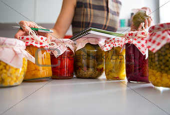 Closeup on jars of pickled vegetables and housewife writing in n