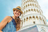 Portrait of happy young woman with map in front of leaning tower