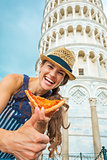 Young woman with pizza showing thumbs up in front of leaning tow