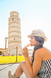 Happy young woman eating pizza in front of leaning tower of pisa