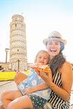 Happy mother and baby girl eating pizza in front of leaning towe