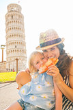 Happy mother and baby girl eating pizza in front of leaning towe