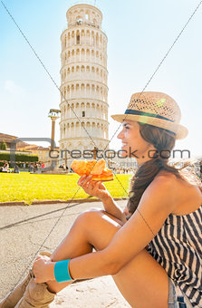 Happy young woman eating pizza in front of leaning tower of pisa