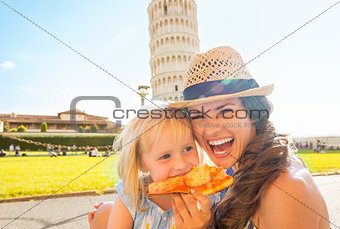 Portrait of happy mother and baby girl eating pizza in front of 