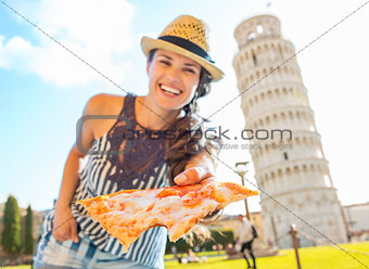Smiling young woman giving pizza in front of leaning tower of pi