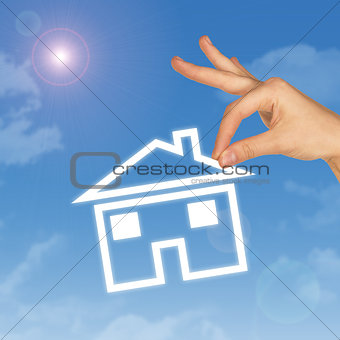 Hand holding house icon. Background of sky, clouds and sun