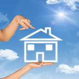 House icon on hand. Background of sky, clouds and sun