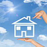 House icon on hand. Second hand points to house. Background of sky, clouds and sun