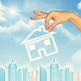 Hand holding house icon. Background of sky, clouds and sun