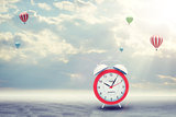 Alarm clock on concrete floor with background of clouds, hot air balloon