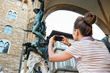 Young woman taking photo of statue perseus with the head of medu