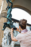 Young woman taking photo of statue perseus with the head of medu