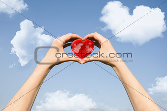 Red heart in hands on the sky