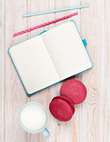 Cup of milk and macarons on white wooden table with notepad