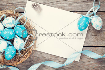 Easter greeting card with blue and white eggs in nest over wood