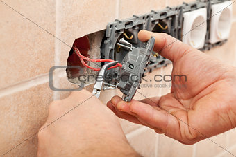 Electrician hands installing wires into a wall fixture