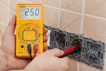 Electrician hands with multimeter measuring the voltage in a wal