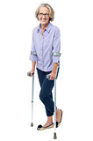 Bespectacled old woman walking with crutches