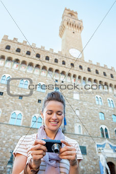 Happy young woman checking photos in camera in front of palazzo 