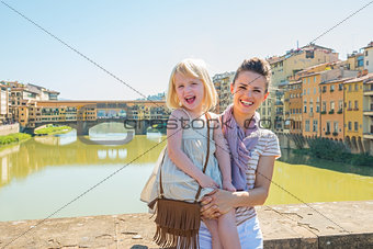 Happy mother and baby girl standing on bridge overlooking ponte 