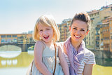 Portrait of happy mother and baby girl standing on bridge overlo