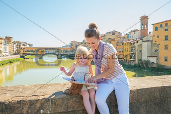 Mother and baby girl sitting on bridge overlooking ponte vecchio