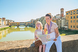 Happy mother and baby girl with map sitting on bridge overlookin