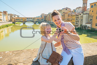 Happy mother and baby girl checking photos in camera on bridge o