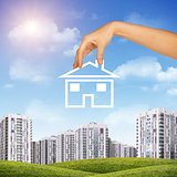 Hand holding house icon. Background of sky , clouds and sun, buildings