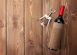 Red wine bottle and corkscrew on wooden table