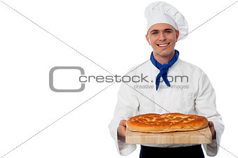 Young baker holds a loaf on breadboard