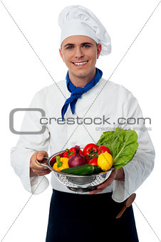 Chef holding fresh vegetables in strainer bowl