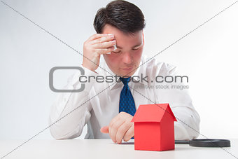 Sad Man with a magnifying glass and paper house