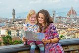 Happy mother and baby girl looking at map against panoramic view
