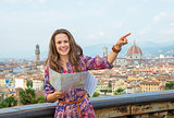 Smiling young woman with map pointing against panoramic view of 