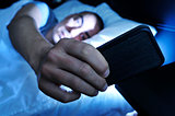 young man looking at the smartphone in bed at night