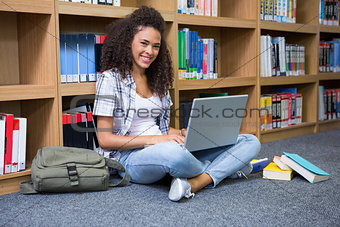 Student sitting on floor in library using laptop