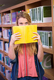 Student covering face with book in library