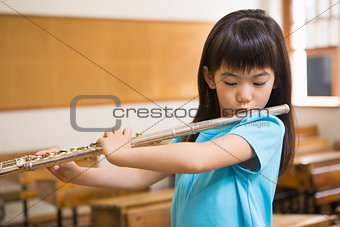 Cute pupil playing flute in classroom