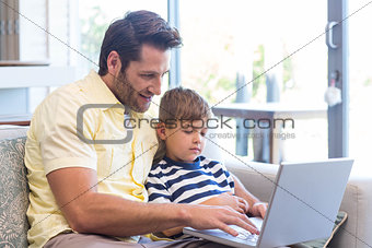 Father and son using laptop on the couch