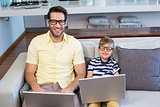 Father and son using laptops on the couch