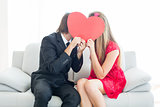 Cute geeky couple kissing and holding heart over faces