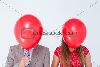 Geeky couple holding balloons in front of their faces