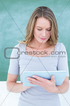 Smiling teacher using tablet pc in front of blackboard