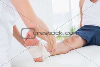 Doctor bandaging her patient ankle