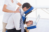 Businessman having back massage while using laptop